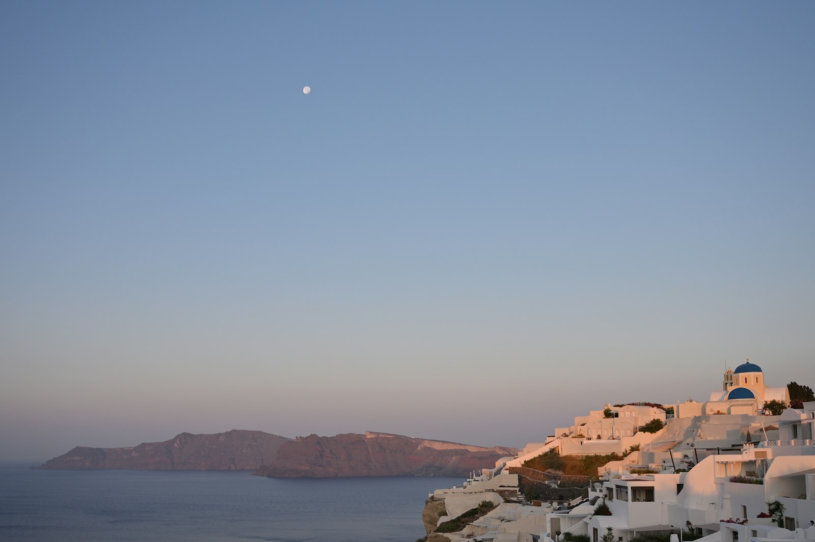 White Oia village cascading down the Santorini cliff with an iconic blue dome and the caldera at blue hour